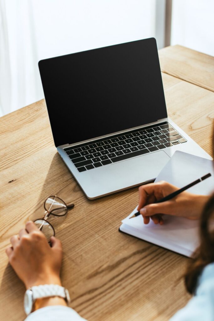 Person writing beside laptop and glasses